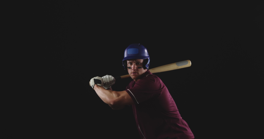 Front view of a Caucasian male baseball hitter, wearing a team uniform, a helmet and stripes of eye black under his eyes, swinging a baseball bat and hitting a baseball, slow motion 