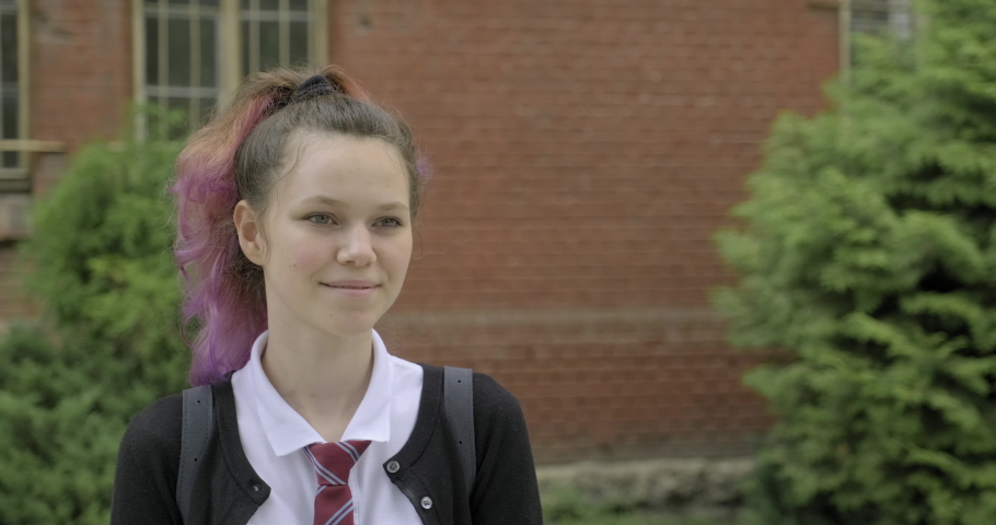 Teenager girl in uniform with backpack walking near school building. Back to school