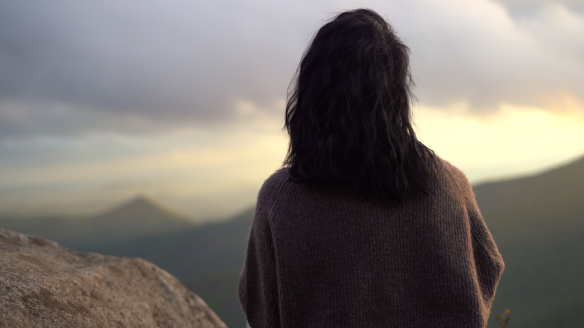 Young woman takes in the stunning panoramic view from the summit of a mountain range -4K