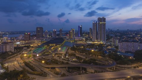 Aerial time lapse of Johor Bahru city with tall buildings in clear sky at sunset and busy traffic on elevated highway leading to CIQ. Day to night. Zoom in motion timelapse. Prores 4K
