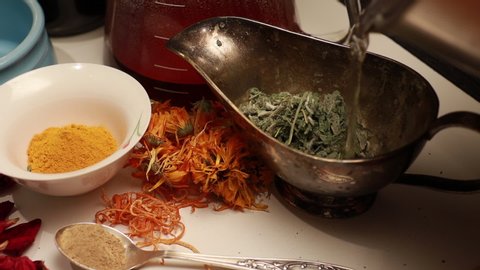 close-up of making sage infusion in an old silver bowl with patina in a composition with dried calendula, ground turmeric and ginger near on the table
