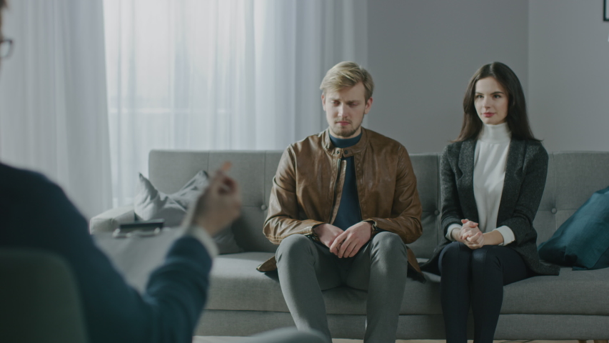 Unfocused Couple on a Counseling Session with Psychotherapist. Focus on Back of the Therapist Taking Notes and Talking: People Sitting on the Analyst Couch, Discussing Relationship Problems | Shutterstock HD Video #1041916771