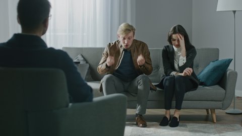 Young Couple on a Counseling Session with Psychotherapist. Back View of Therapist Taking Notes: Angry and Aggressive Boyfriend loses Temper, Starts a Fight, Shouts at His Suffering Girlfriend