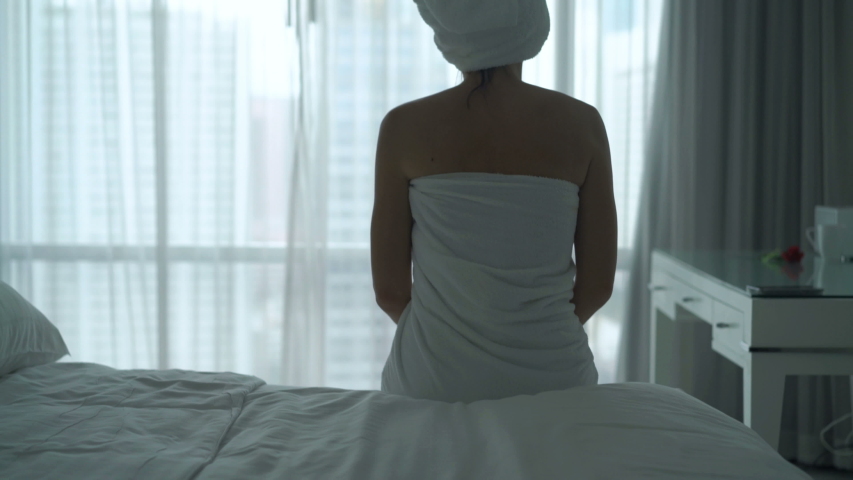 Young beautiful woman in towel stretching arms sitting on bed