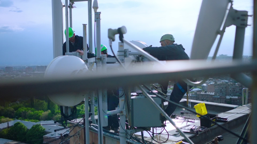 Workers servicing cellular antenna in front of city . Contractors working on a telecommunications mast at height .  Telecommunication technician working on top of cellular antenna. The cell tower. Royalty-Free Stock Footage #1041919225