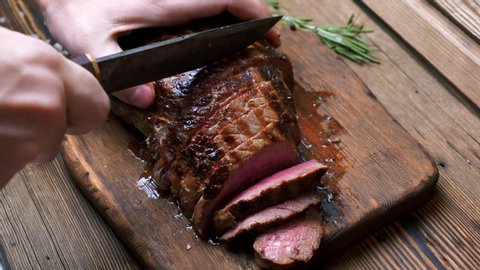 Chef with Vintage Knife Cuts of Grilled Beef Steak on Rustic Cutting Board on Wooden Background. Juicy Sliced Rib Eye Steak with Salt. Concept of Delicious Meat Food