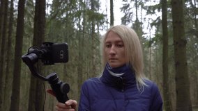 Young girl blogger makes video with her phone and gimbal in forest on nature.