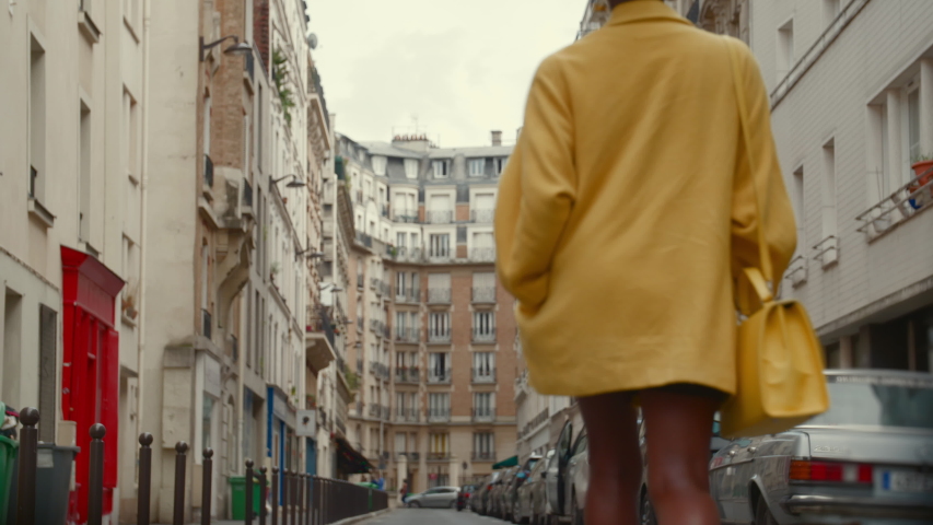 Low angle view of an exotic, stylish woman dressed in classy bright colored clothing walking down a city street in Paris, France. Fashion model struts boldly down an empty street. | Shutterstock HD Video #1041934066