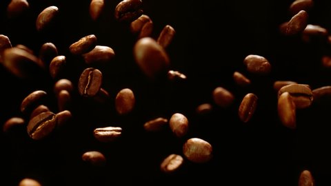 Roasted coffee beans fly and spin on a black background in slow motion