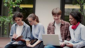 Medium shot of young cheerful multinational students joyfully studying with laptop in university campus