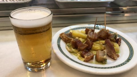 Beer glass with tapas food, typical in Spain. Beer and tapa on a bar counter, Spanish tradition. Typical tapa of beer and roasted potatoes with bacon in Spain.