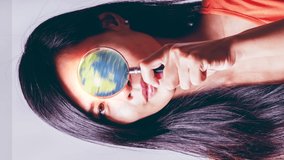 Asian American woman looking through magnifying glass with glowing spinning globe cinemagraph, vertical format video