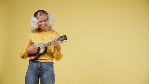 A video of a woman playing a colorful ukulele and at the same time singing with a smile on her face showing off her perfect while teeth.