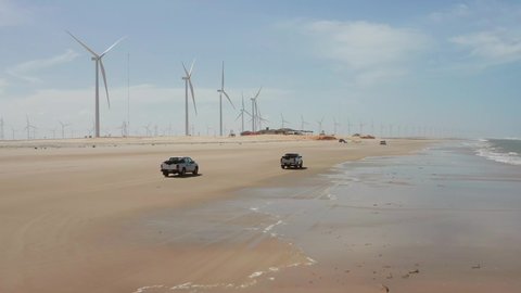 Atins / Brazil - 11 24 2018: Pickup trucks driving on the beach to Atins, passing by a new windturbine park.