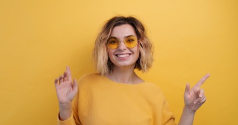 Portrait Happy Woman Smiling Dancing to Music Rhythmically to Beat Moving her Hands in Yellow Sweater Yellow Background Slow Motion in Yellow Glasses . Monotone. Positive Emotions of People. Freedom