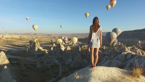Woman Walking to Edge of Rock and Looking at Hot Air Balloons, Cappadocia, Turkey.