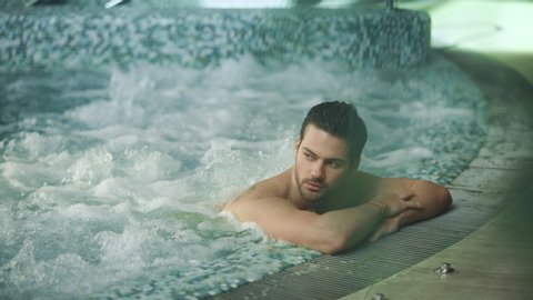 Sexy man relaxing in jacuzzi spa at modern hotel. Young guy resting in whirlpool bath at wellness center. Attractive man enjoying hydrotherapy at spa resort.
