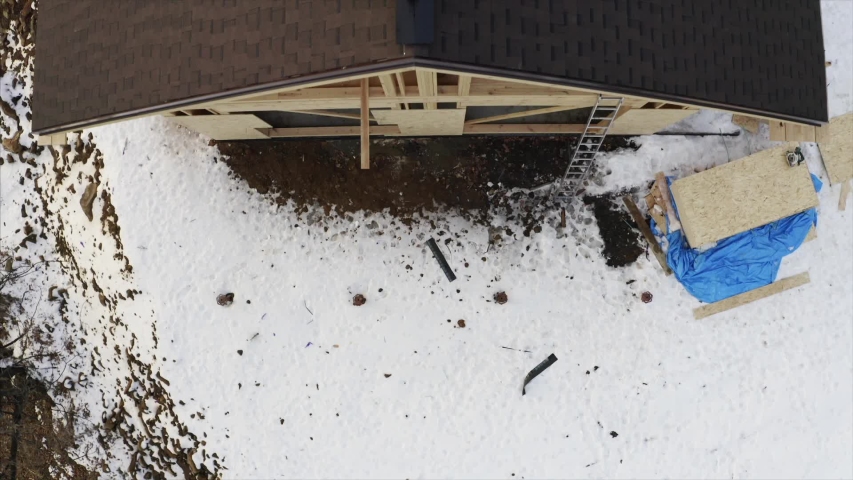 Top aerial view, flying above the house under constuction and builder in safety harness on the roof finishing the roof ridge