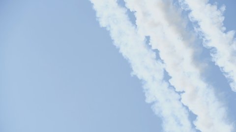 One military plane makes a loop around other planes at an air show, releasing smoke strips. Airplane makes unusual maneuvers at an airshow. Planes are flying fast.