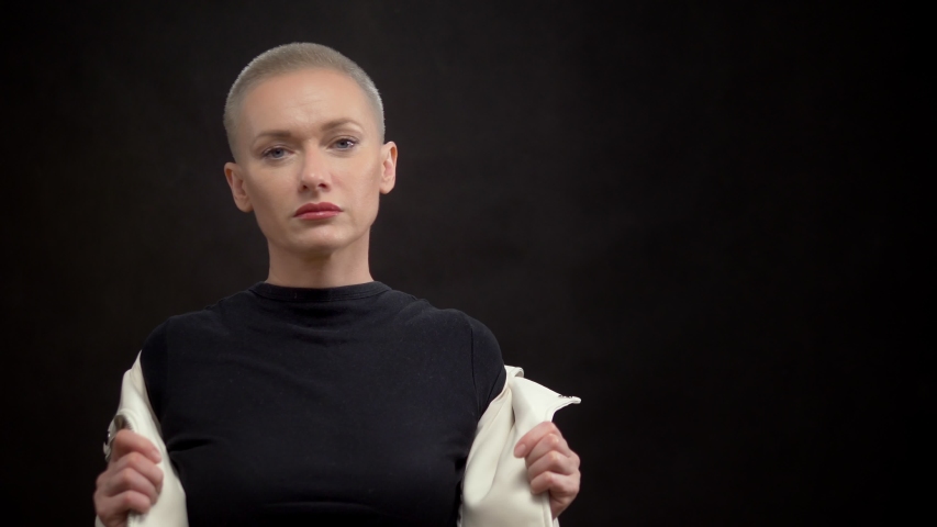 beautiful stylish blond woman with short hair on a black background in a white leather jacket. looking at the camera.