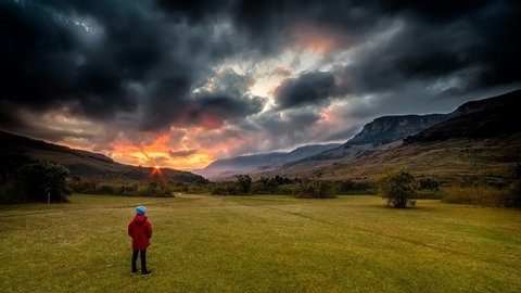 A boy in a red jacket watching the sunrise and the storm clouds clearing in a national park in South Africa