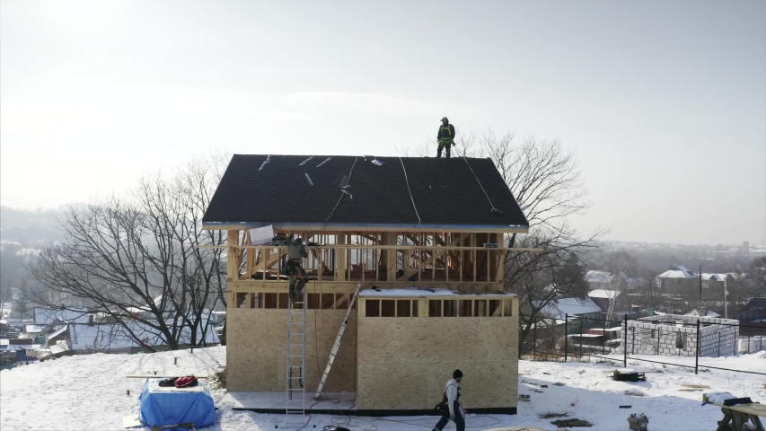 Aerial view of residential house under constuction and tiler in safety harness on the roof top. Bright sunny day