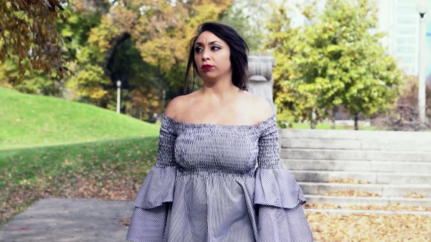 beautiful Latina woman wearing a trendy skirt is walking around causally in a lush green park located in downtown Chicago. the leaves slowly change color in the serene garden landscape