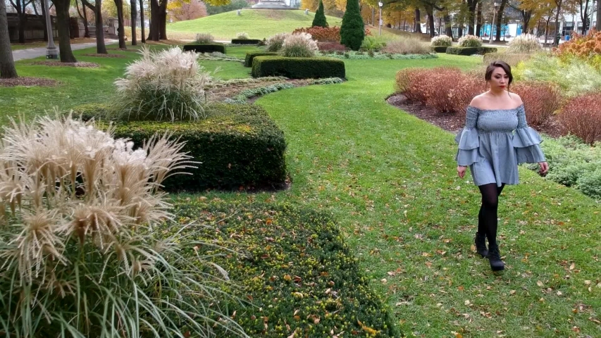 beautiful Latina woman wearing a trendy skirt is walking around causally in a lush green park located in downtown Chicago. the leaves slowly change color in the serene garden landscape