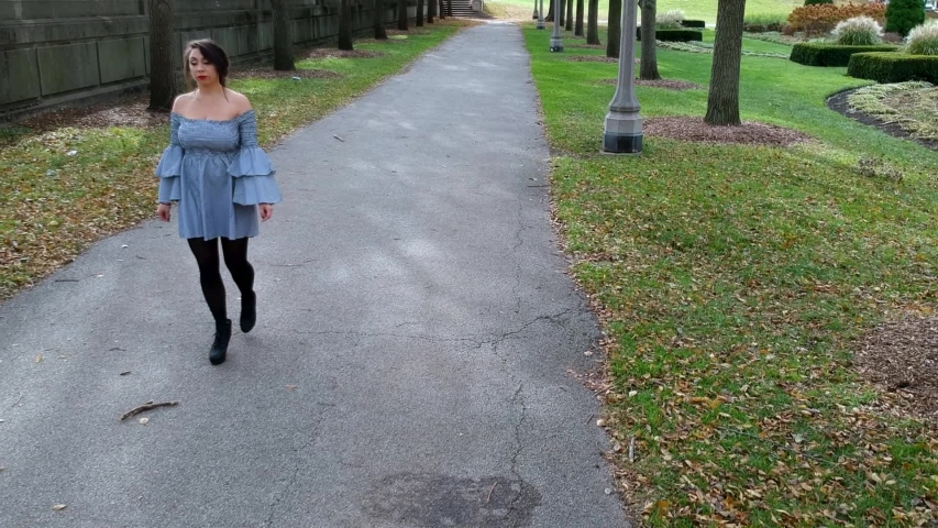 beautiful Latina woman wearing a trendy skirt is walking around causally in a lush green park located in downtown Chicago. the leaves slowly change color in the serene garden landscape