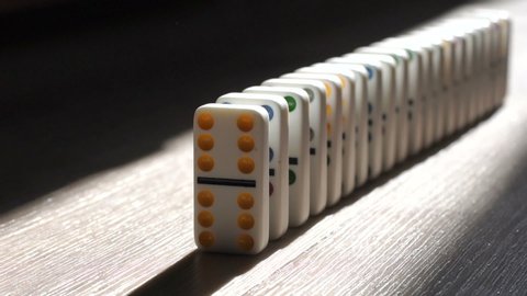 A men pushes a Domino and starts a chain reaction on the floor in a patch of sunlight. Sun ray. Close-up. Slow motion. Dominoes. Chain reaction. The Domino Principle. Board game. Falling dominoes.