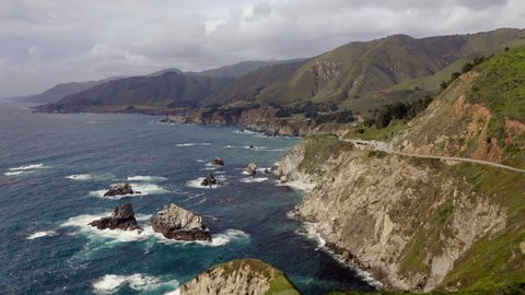 Stunning aerial view over the rocky ocean coast. Beautiful ocean water of various shades of blue meets the rocky shore. Most scenic stretch of undeveloped coastline in USA, known as Big Sur. 4K