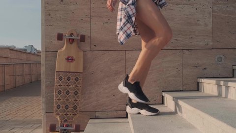The feet of a young woman in black sneakers, shorts and a plaid shirt climb the stairs, a stone wall in the background. Slow motion. Tracking camera on the object.
