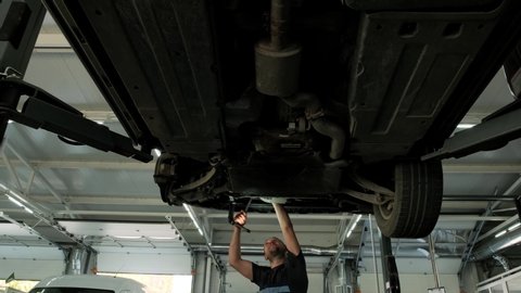 Auto mechanic working underneath car lifting machine at the garage. Auto repair shop, Car service, repair.    
