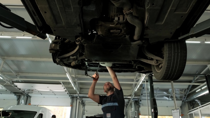 Auto mechanic working underneath car lifting machine at the garage. Auto repair shop, Car service, repair.     | Shutterstock HD Video #1041998170
