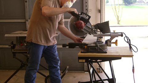 A tradesman or handyman homeowner type using a power miter saw to cut a board for a home improvement project.