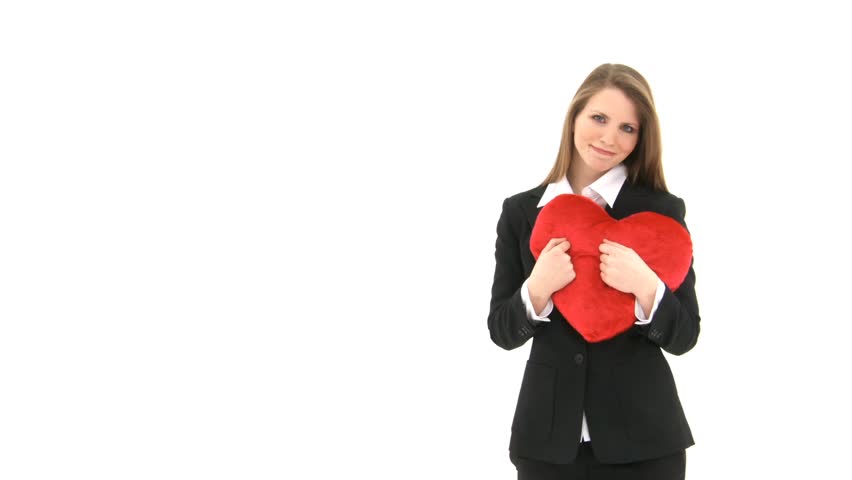 Woman stands in front of white background cuddling with a red heart pillow