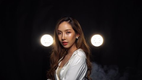A sultry Asian model shows her new face after rhinoplasty in a fashion photo shoot, studio backlit smoke fog dark background, medium shot 4k