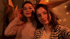 Happy two beautiful girls take a selfie on the background of a Christmas tree.  Call to parents. Call friends. Video chat. Christmas party. Family party. Happy millennials. Happy girls enjoying party.