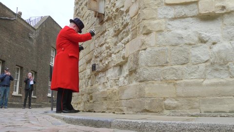 London, UK - April, 2019: The bell ringer rings the bell at the Tower of London at a specific time. Compliance with the traditions of British culture. A beefeater in a red coat rings the bell.