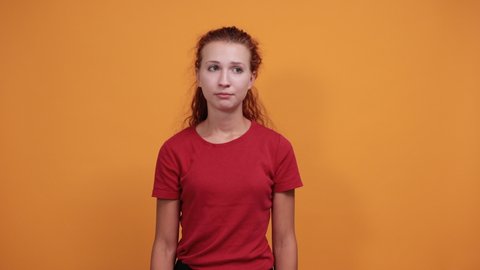 Pretty young lady in red shirt spreads hands, looking disappointed isolated on orange background in studio. People sincere emotions, sport concept.