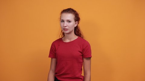 Disapointed young woman in red shirt isolated on orange background in studio doing stop no gesture. People sincere emotions, health concept.