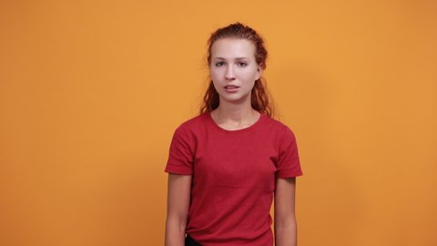 Pretty young lady in red shirt keeping hand down, laughting, smiling isolated on orange background in studio. People sincere emotions, health concept.