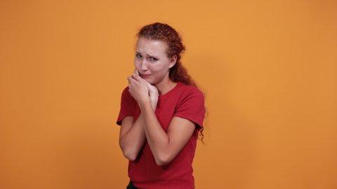 Attractive young lady in red shirt keeping hand on mouth, toothache, pain isolated on orange background in studio. People sincere emotions, painful concept.