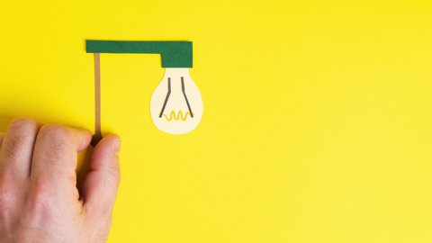 Man hand turns on incandescent light bulb, stop motion animation. Paper art. Business concept.