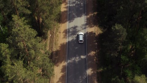 One white wagon car driving / travel on freeway through dense forest corridor at summer sunny day - Aerial drone view