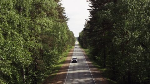One black wagon SUV car driving in  freeway through dense forest corridor at summer sunny day - Aerial drone view