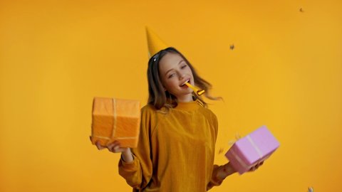 teenager holding gifts and blowing in party horn isolated on yellow