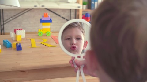 Close-up of a preschooler looks in the mirror and repeats the sounds at the reception of a speech therapist