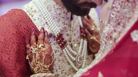 Pakistan - July 2018: Indian Pakistani newlywed couple, wearing traditional red and golden jewelry, shares a romantic moment at their royal wedding – Close-up shot in HD.