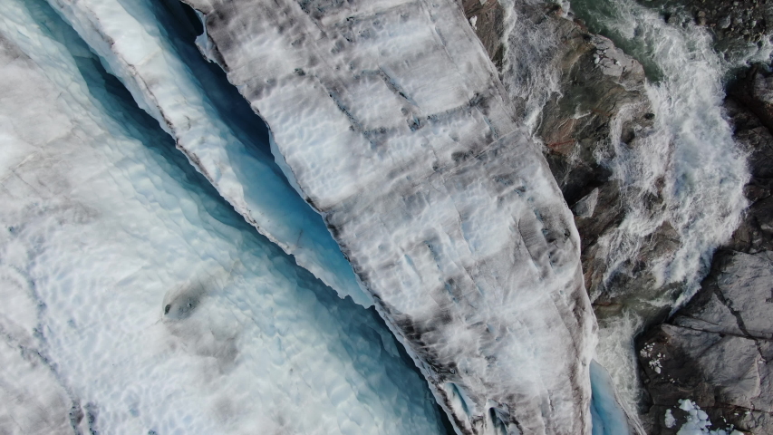 Aerial drone tilt view of the glacier of Sam Ford Fjord, Canada, near Greenland, showing ice melting from the glacier and a water stream of the nearby river flowing in the arctic sea